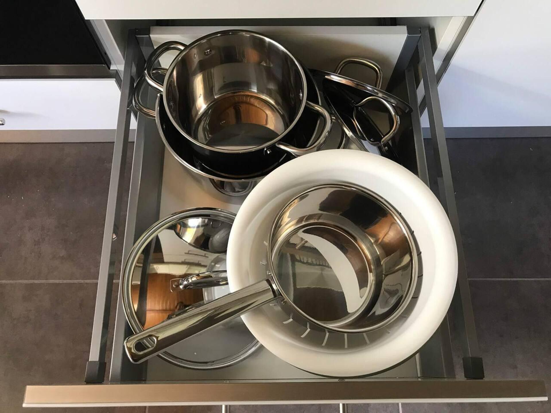 A kitchen drawer with stainless steel cookware including pots, pans, and a frying pan.