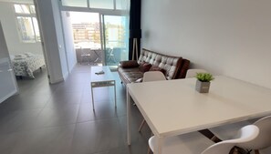 A modern living room with a sofa, a dining table, and a small potted plant. - Renovated Apartment by the Beach and Yumbo Centre (San Bartolomé de Tirajana)