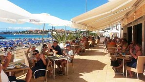 Un restaurante frente a la playa con terraza, sombrillas y vistas al mar.