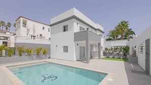 Un edificio moderno con piscina, mobiliario exterior y palmeras.