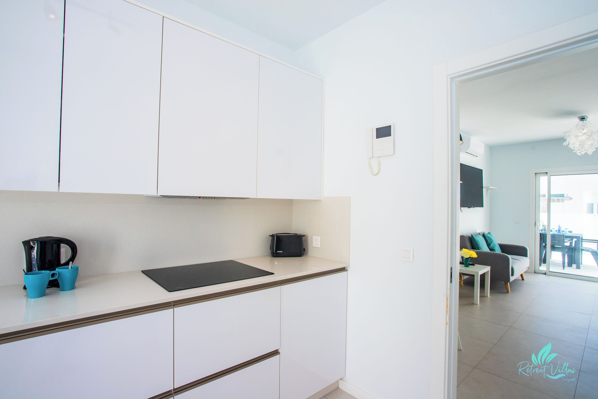 A modern kitchen with white cabinets, a black countertop, and a coffee maker. There is a dining area visible through an open door.