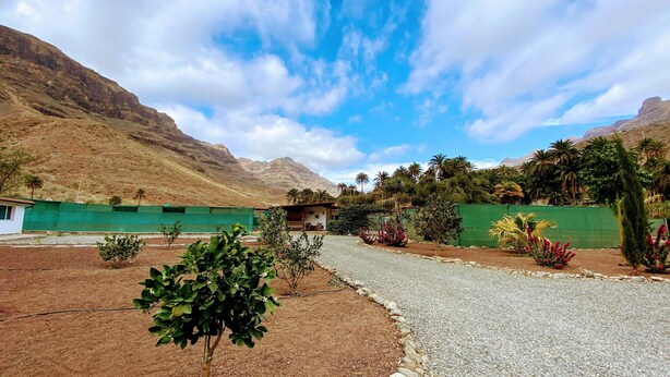 A residential area with a gravel driveway, green fences, and a house with a small porch. - Large Country House Near Maspalomas & Fataga (San Bartolomé de Tirajana)