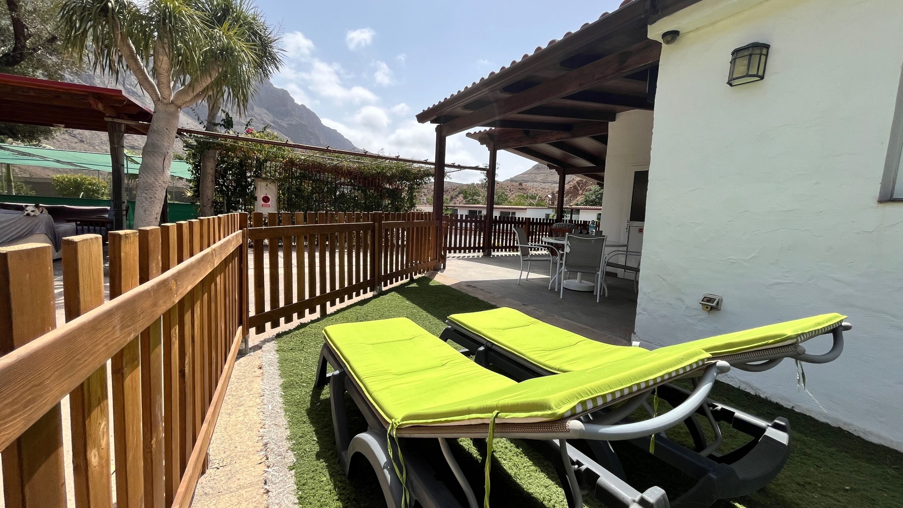 Un patio con dos sillones de descanso, cercado por una valla de madera, y un espacio de estar cubierto.