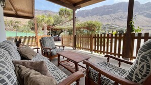 A covered outdoor seating area with wooden furniture, a wooden fence, and a view of mountains in the background. - Large Country House Near Maspalomas & Fataga (San Bartolomé de Tirajana)