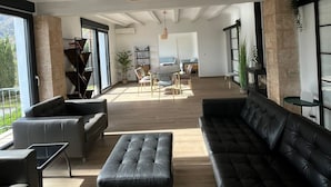 A spacious living area with a modern design, featuring a black leather sofa, a black ottoman, and a dining table with chairs. There is a large window providing a view of the outdoors. - Modern 5 Bed Villa in Javea (Javea)