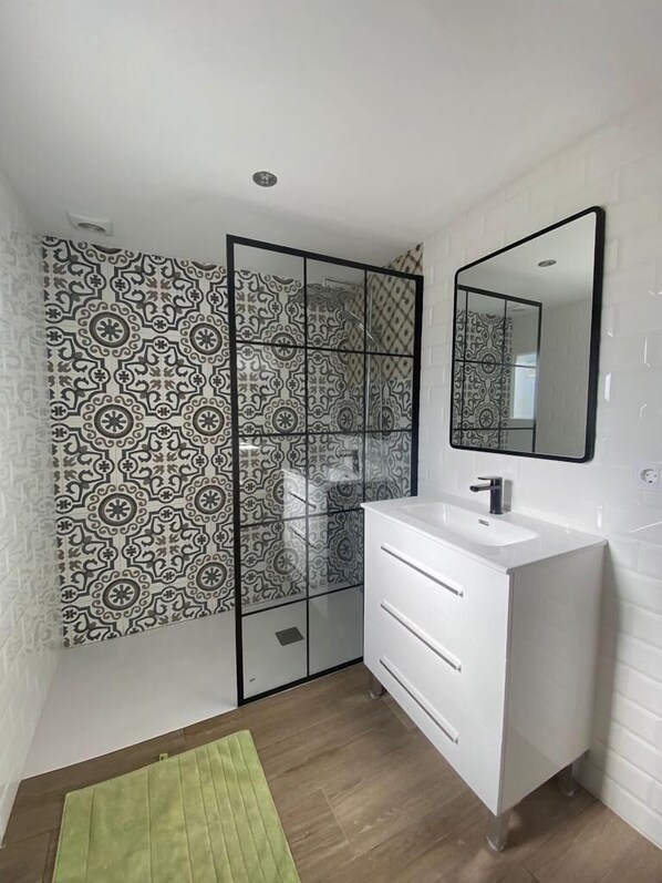 Une salle de bain avec un meuble-lavabo blanc, un miroir, des carreaux décorés et un tapis vert sur le sol.
