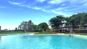 Una piscina con agua azul cristalina, rodeada de vegetación y edificios.