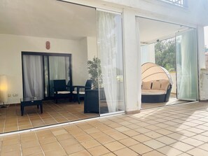 Ein sonnendurchflutetes Zimmer mit Glastür, gepolsterten Sitzmöglichkeiten und einem Topf mit Pflanze.