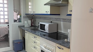 Une cuisine de taille réduite, avec des meubles blancs, un four à micro-ondes, une cuisinière et un réfrigérateur.