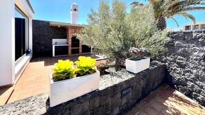 Eine Terrasse im Freien mit einem gemauerten Grill, Blumentöpfen und einer Steinmauer.