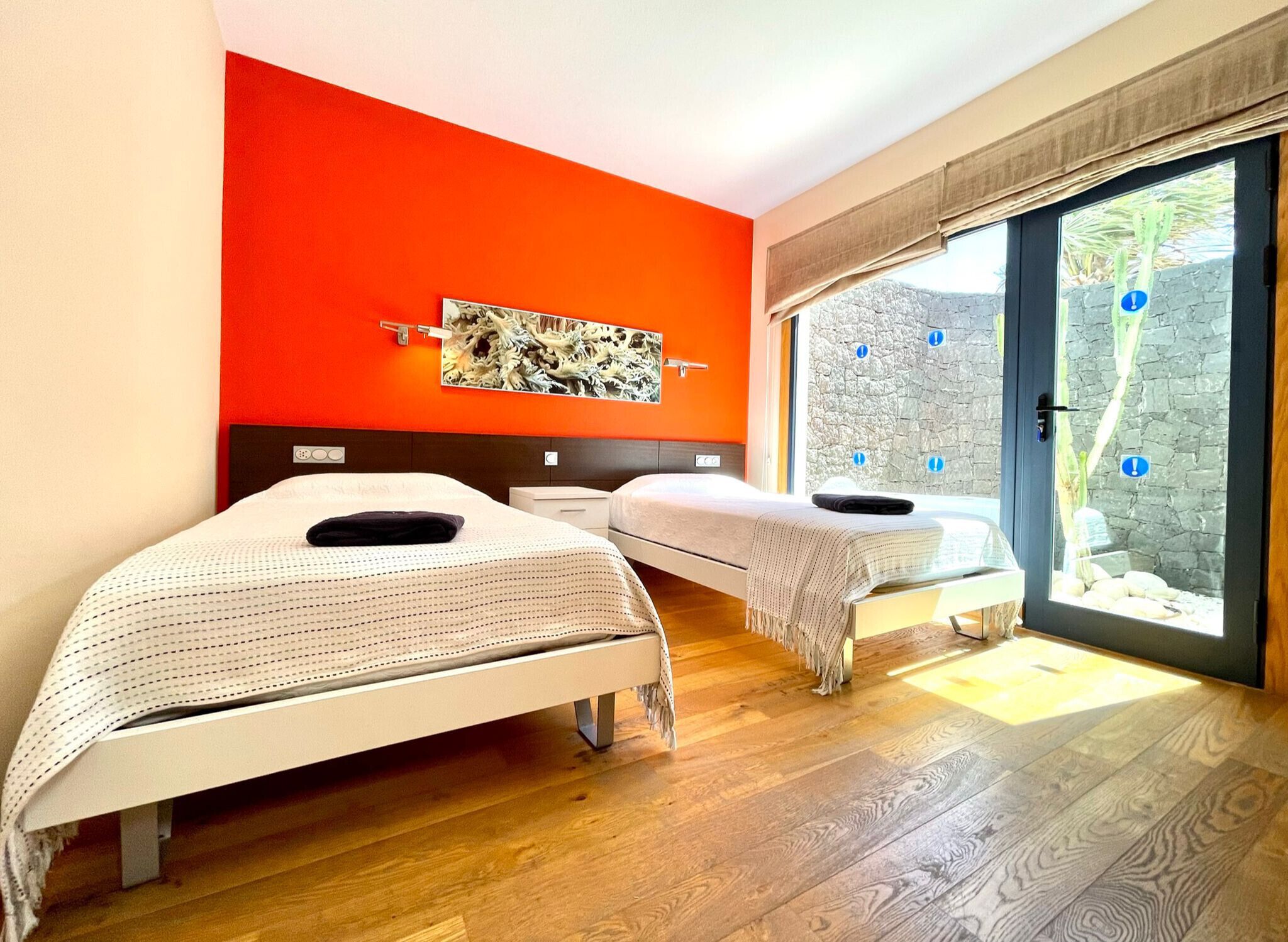 Une chambre avec deux lits, un mur d’accent rouge, un mur en pierre à l’extérieur et une porte-fenêtre coulissante.