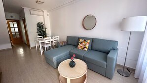 A modern living room with a grey sectional sofa, a round wooden coffee table, a dining table with chairs, and a potted plant. - 2 Bed House - Sleeps 4 - Pool - Terrace - Parking (Pulpi)