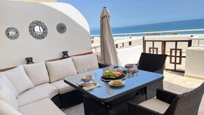 Uma área de refeições com uma mesa posta para dois, rodeada por cadeiras de vime e um sofá.
