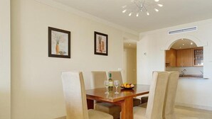 Uma sala de jantar com uma mesa de madeira e quatro cadeiras, uma garrafa de vinho e duas molduras com quadros na parede.