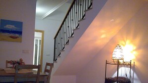 Un coin repas avec une table et des chaises, un escalier et une lampe fixée au mur.