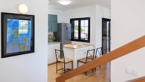 A modern kitchen with white cabinets, a stainless steel refrigerator, and a wooden dining table with two chairs. - Stunning 4-bed Villa in Playa Blanca (Yaiza)