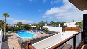 A rooftop swimming pool with lounge chairs, surrounded by palm trees and a clear sky. - Stunning 4-bed Villa in Playa Blanca (Yaiza)