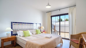 A hotel room with a large bed, a wicker chair, a nightstand with a lamp, and a colorful headboard. - Stunning 4-bed Villa in Playa Blanca (Yaiza)