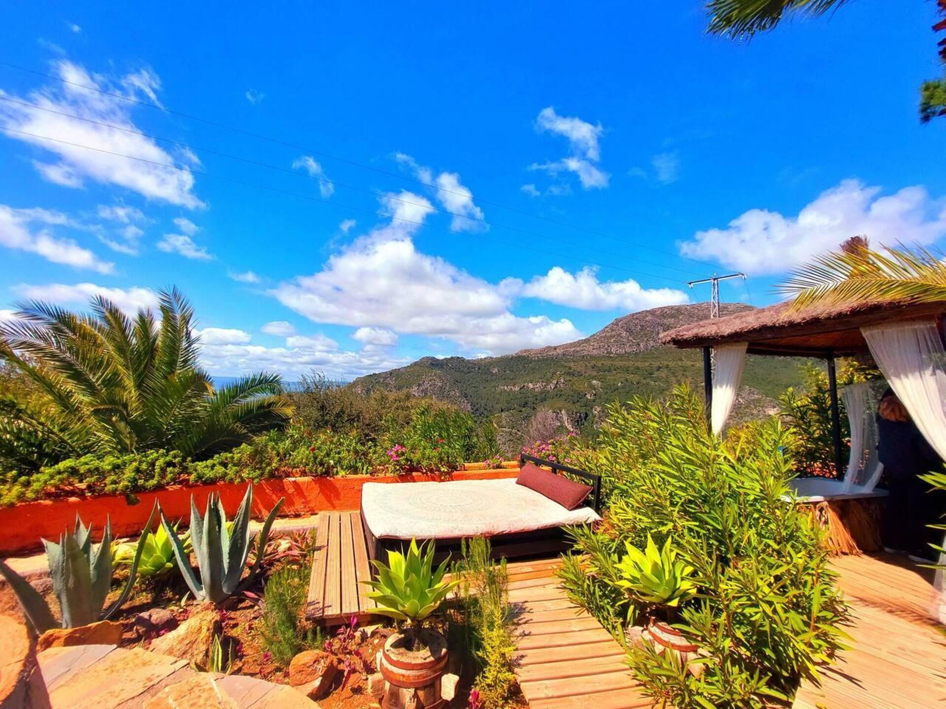 A rooftop garden with a wooden deck, potted plants, and a thatched-roof structure.