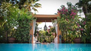 Un espace piscine avec une eau d’un bleu limpide, entouré d’une végétation luxuriante et de plantes en fleurs.