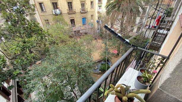 A balcony with a view of a courtyard, potted plants, and a building with multiple balconies.