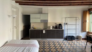 A compact hotel room with a bed, a kitchenette, a patterned floor, and a wooden ceiling.