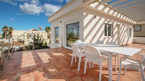 A patio with a white table and chairs, a glass door, and a view of neighboring buildings. - 3-bed Villa Sleeps 8 With Private Pool (Santa Pola)