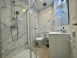 Baño con ducha de vidrio, inodoro y lavamanos con espejo.