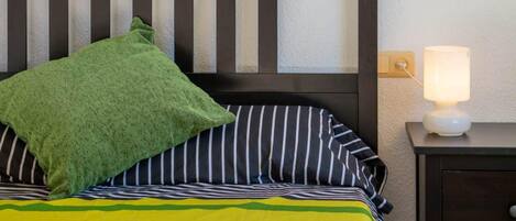 A bed with striped bedding, a green pillow, and a bedside lamp.