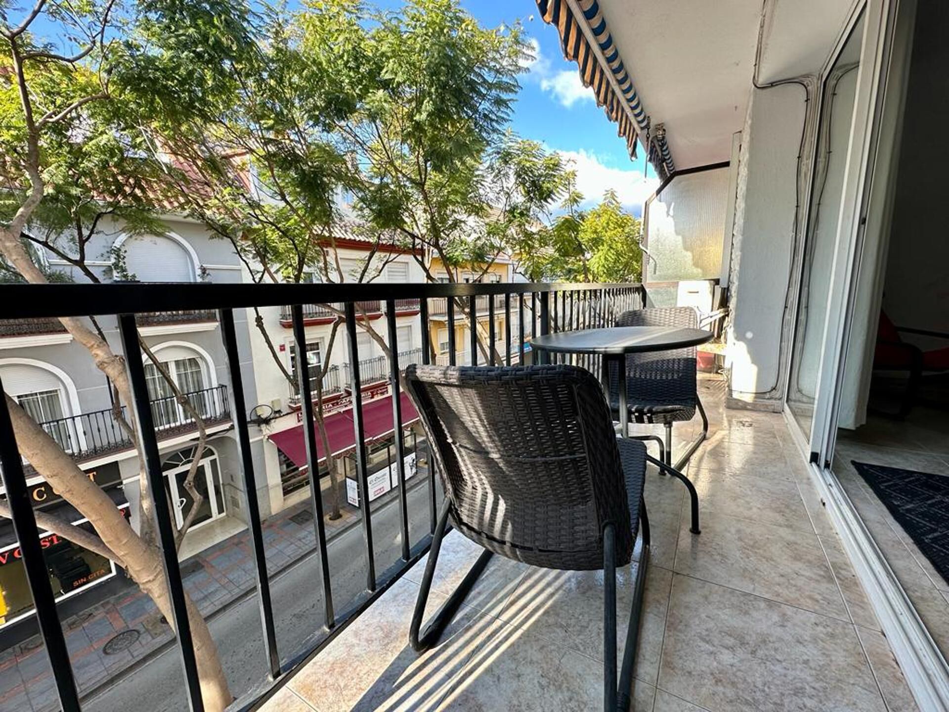 A balcony with a table and chairs, overlooking a street with buildings and trees.