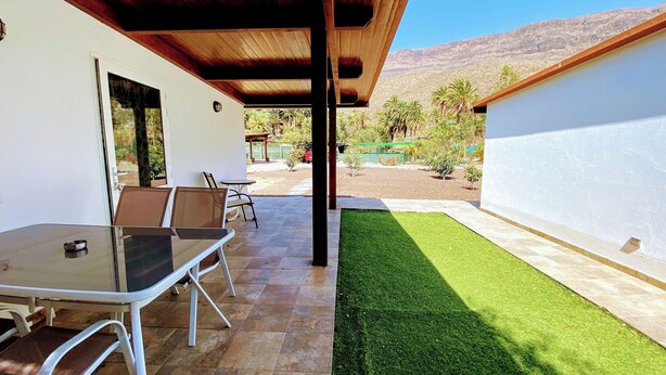 Une terrasse extérieure avec une table et des chaises, un espace abrité et une pelouse bien entretenue.