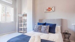 A bedroom with a bed, pillows, a headboard, a wall art piece, a shelf unit, and a small table. - Remarkable 3 Bedroom Apartment in L'eixample (Valencia)