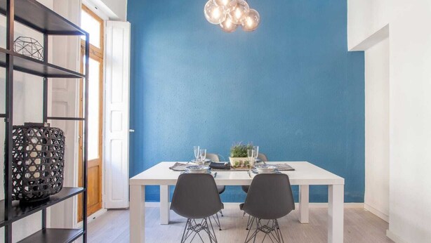 A dining area with a white table set for two, a blue accent wall, and a hanging light fixture. - Remarkable 3 Bedroom Apartment in L'eixample (Valencia)