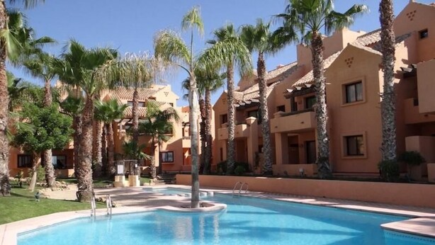 Piscina rodeada de palmeras y edificios de varios pisos con balcones.