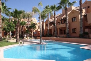 A swimming pool surrounded by palm trees and multi-story buildings with balconies.