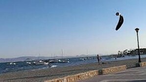 Escena costera con cielo despejado, un paseo marítimo y barcos en el agua.