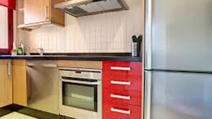 Una cocina con gabinetes de madera, una campana extractora de acero inoxidable, un horno empotrado y una encimera roja.