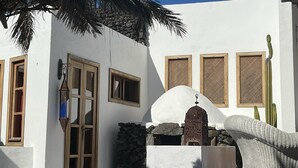 Un edificio bianco con un muro in pietra, persiane di legno e un cactus.