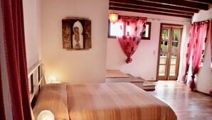 Una camera da letto con un letto, un comodino, una lampada a parete, una finestra con tende e una porta che dà sull'esterno.