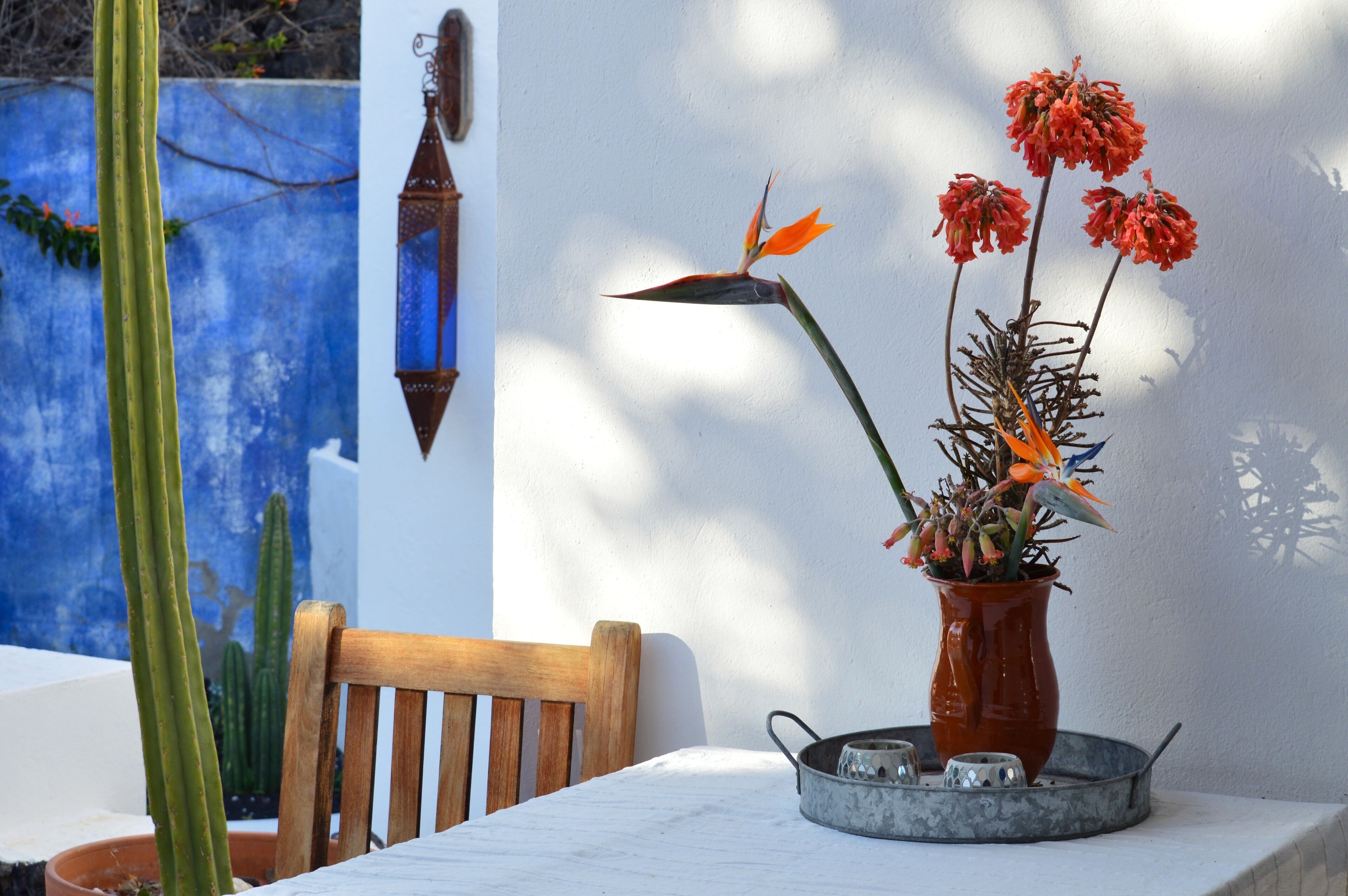 A table with a vase of flowers, a wooden chair, and a metal tray with salt and pepper shakers.