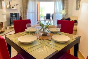 A dining table set for four with white plates, red chairs, and a central plant.