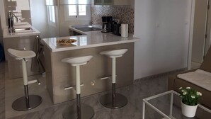 A modern kitchen with a central island, two bar stools, a coffee machine, and a potted plant. - Apartment Sleeps 4 Near Beach (Fuengirola)