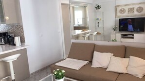 A modern living room with a sofa, a coffee table, and a TV. There is a kitchen area with a countertop and appliances. - Apartment Sleeps 4 Near Beach (Fuengirola)