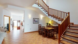 A spacious living area with a dining table, chairs, and a wooden staircase.