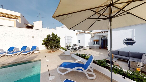 A poolside area with lounge chairs, a table with chairs, a small tree, and a sofa.