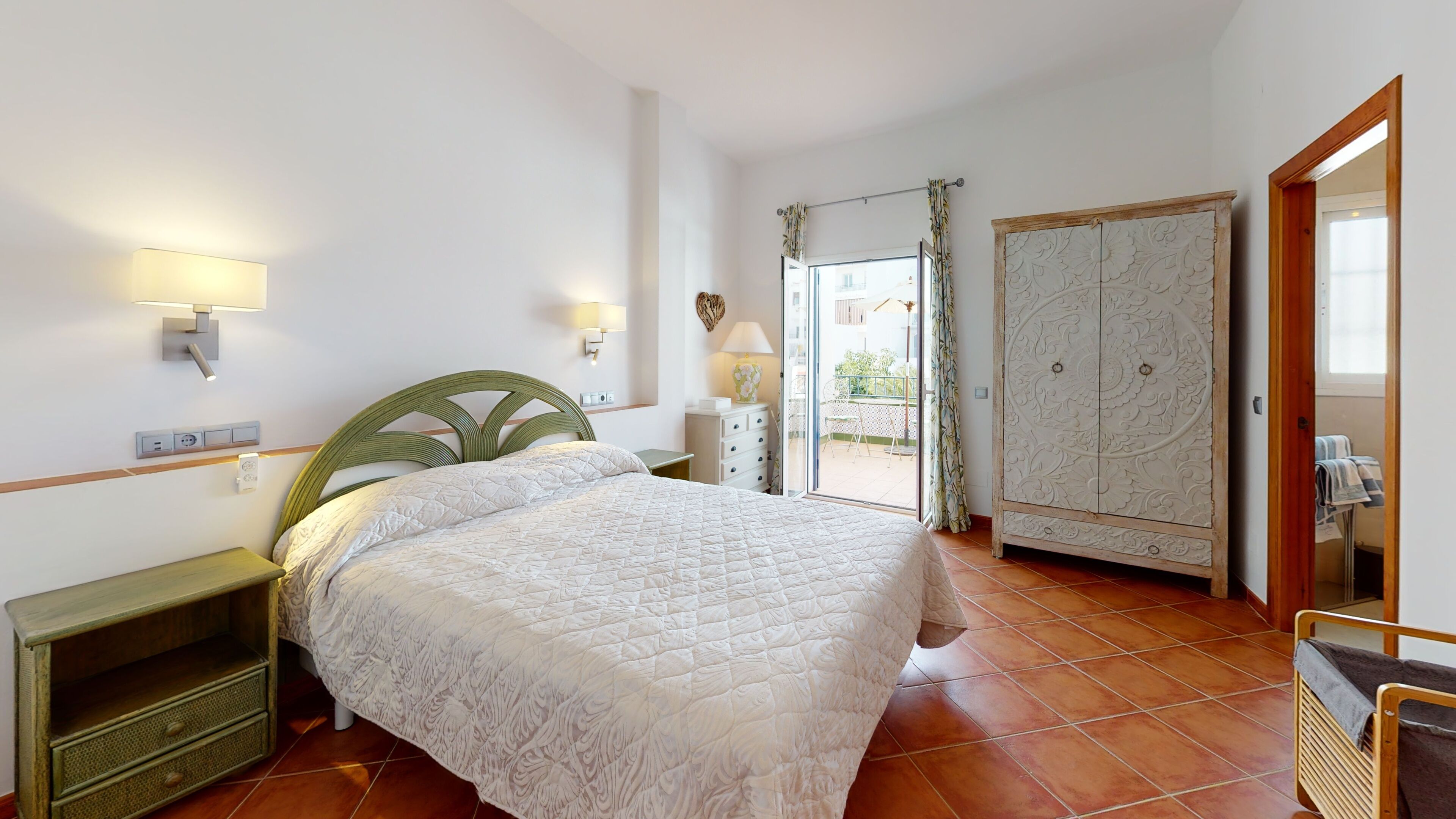 A bedroom with a bed, bedside tables, a wardrobe, and a view to the outside.
