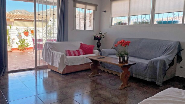 A living room with a sofa, a coffee table, and a sliding glass door leading to an outdoor area with potted plants. - Central Attic Apt Sleeps 4 With Patio (Almunecar)