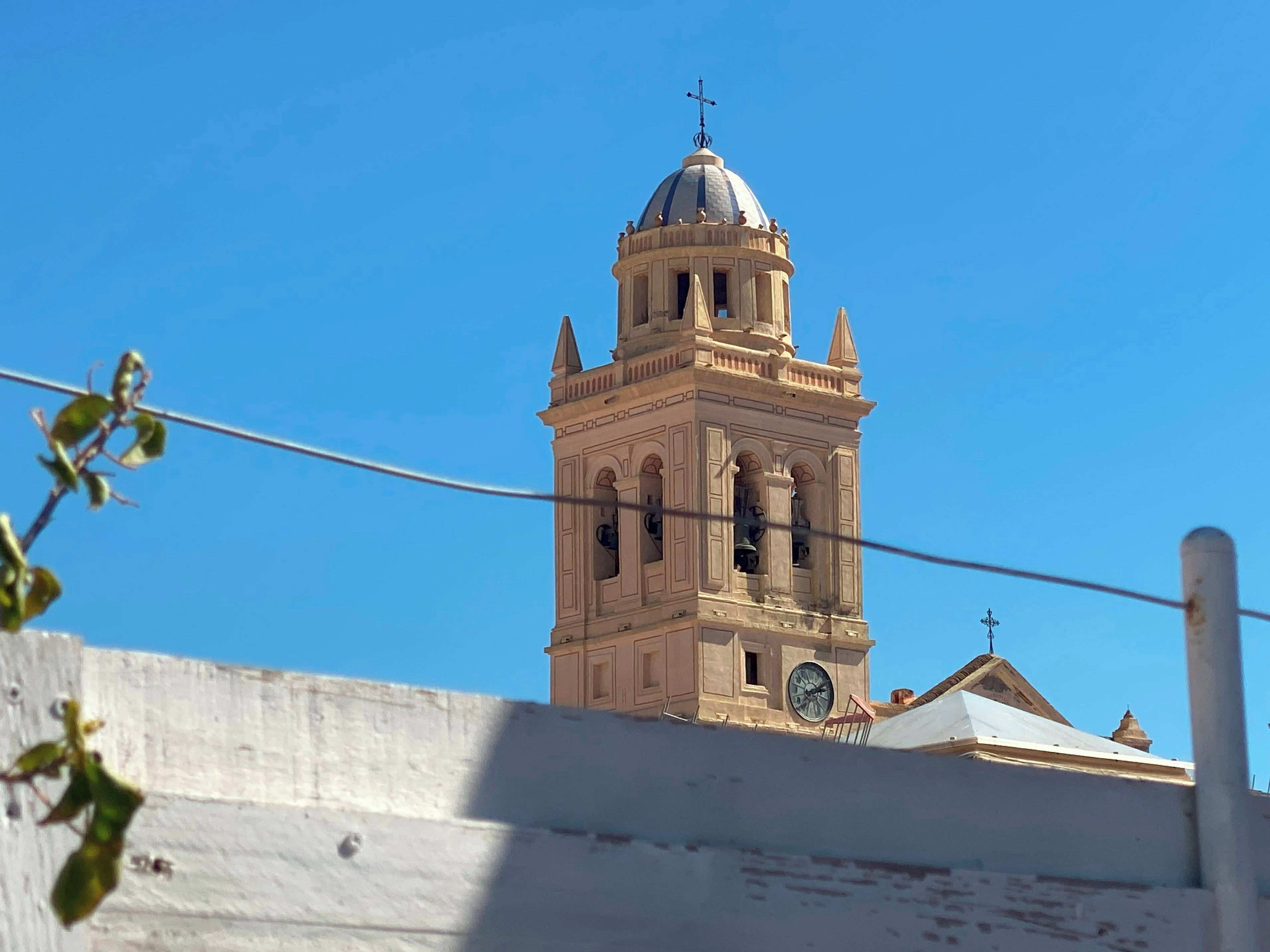 A tall, beige church tower with a cross on top, a clock, and a dome.