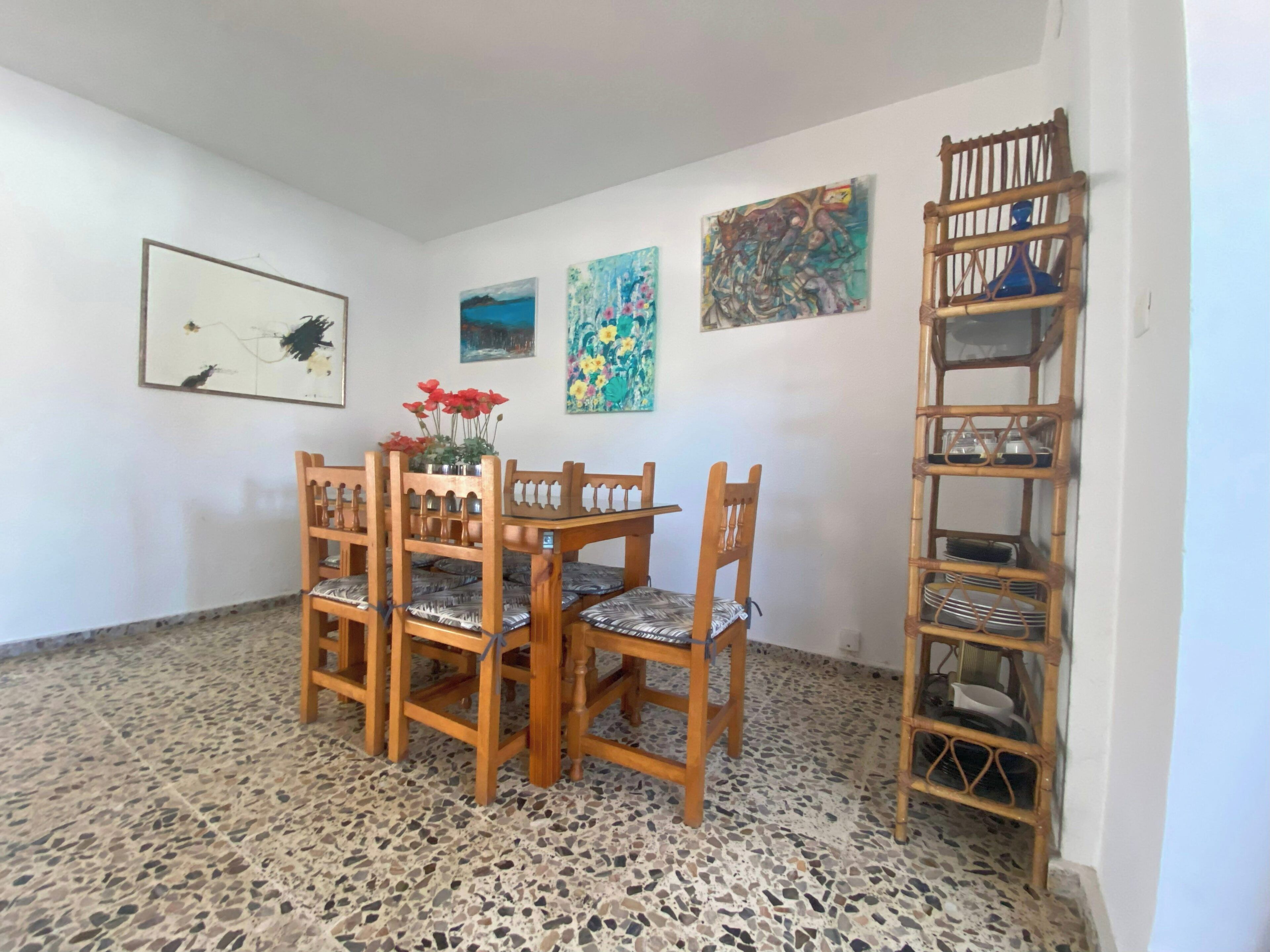 Un comedor con mesa y sillas de madera, suelo de baldosas y una estantería de bambú.