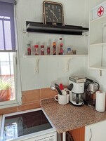 Una cocina con cafetera, un reloj y diversas especias en los estantes.